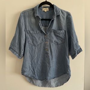 Blue denim collared shirt with white dots. Buttons down front, roll up sleeves
